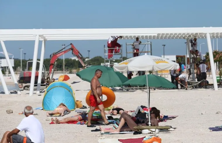 Iako je plaža u &scaron;ibenskoj Brodarici, tzv. Rezali&scaron;tu trebala biti otvorena 15. lipnja, radovi su jo&scaron; u punom jeku. 
Bageri i suncobrani, radnici i kupači zajedno su u srcu sezone na plaži. 
Photo: Dusko Jaramaz/PIXSELL