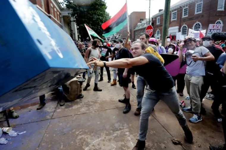 CHARLOTTESVILLE, VA - AUGUST 12: An anti-fascist counter-protester hurls a newspaper box toward white nationalists, neo-Nazis and members of the "alt-right" during the "Unite the Right" rally outside Lee Park August 12, 2017 in Charlottesville, Virginia. After clashes with anti-fascist protesters and police the rally was declared an unlawful gathering and people were forced out of Lee Park, where a statue of Confederate General Robert E. Lee is slated to be removed.   Chip Somodevilla/Getty Images/AFP