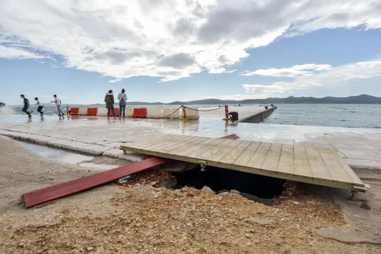 Inače prekrasna zadarska riva sinoć je razornim djelovanjem valova viskih i 4 metra te&scaron;ko o&scaron;tećena. Mul je gotovo u potpunosti potpuno uni&scaron;ten, a od prethodnih juga podlokana riva na mjestima je razrovana poput razbacanih kockica koje opet treba složiti na svoje mjesto. O&scaron;tećenja se vide i kod instalacije Morske orgulje a prve procjene govore da se radi o milijunskim &scaron;tetama.