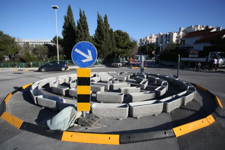 Kružni tok u Bračkoj ulici u Splitu sastavljen je od velikih betonskih žardinjera za cvijeće poslaganih u krug. Posude su prazne.