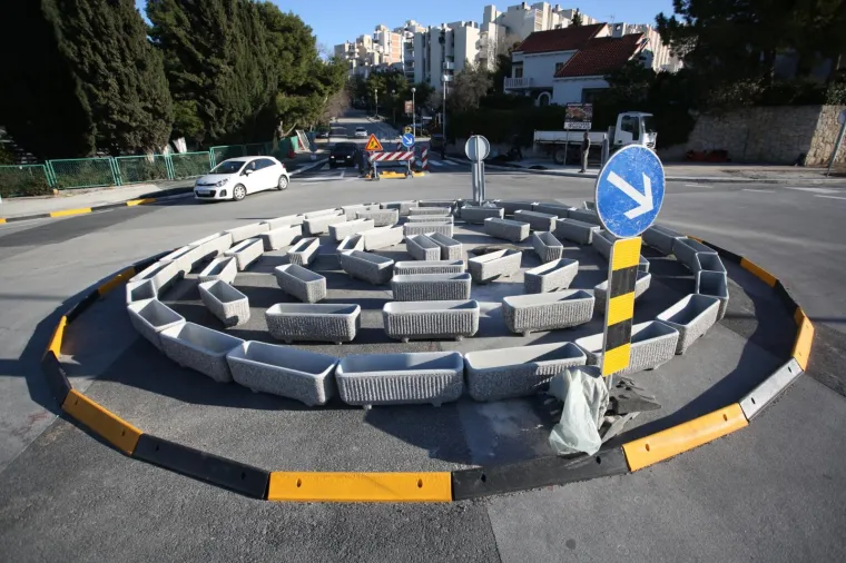 Kružni tok u Bračkoj ulici u Splitu sastavljen je od velikih betonskih žardinjera za cvijeće poslaganih u krug. Posude su prazne.