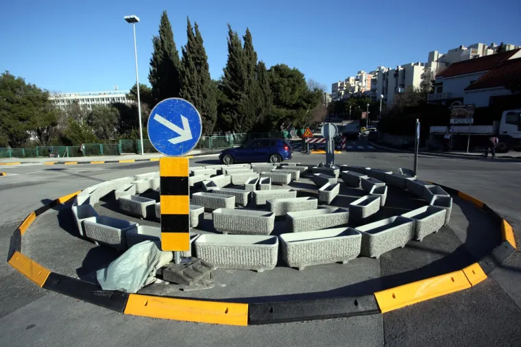 Kružni tok u Bračkoj ulici u Splitu sastavljen je od velikih betonskih žardinjera za cvijeće poslaganih u krug. Posude su prazne.