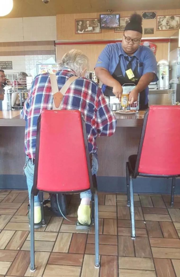 Konobarica pomaže gostu pri rezanju doručka jer je on izgubio moć u rukama.