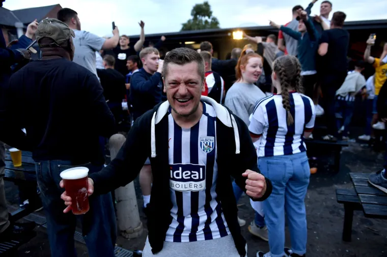 Momčad West Bromwich Albiona koju vodi hrvatski trener Slaven Bilić sljedeće sezone će igrati Premierligu. Baggiesi su u posljednjem kolu Championshipa na svojem terenu odigrali 2:2 s QPR-om i osvojili drugo mjesto na kraju sezone i izravan plasman u elitno društvo.
Utakmica je zbog epidemioloških mjera odigrana pred praznim tribinama, a navijači su izvan stadiona i ispred pubova proslavili veliki uspjeh svoje momčadi.
Foto: Profimedia