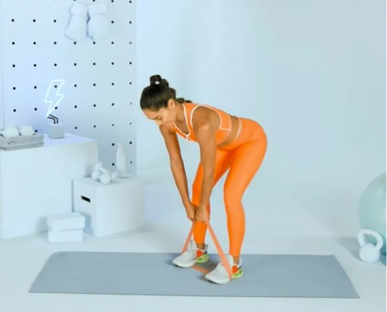 Deadlift: Nakon samo jedne serije, primijetit ćete da su vam gluteusi čvršći, da izgledaju veće,kaže on. Gluteusi su najveća mišićna skupina vašeg tijela, a ovaj ih pokret jako pogađa.
Kako izvesti vježbu? Zamotajte otpornu traku ispod stopala i držite njezine krajeve rukama s ispruženim rukama. Počnite stajati sa stopalima u širini kukova i lagano savijenim koljenima. Ne mijenjajući savijanje koljena, savijte se u kukovima i spustite torzo dok ne bude gotovo paralelan s podom. Zastanite, a zatim podignite trup natrag u početni položaj. To je jedno ponavljanje. Ponovite tri serije po 10 ponavljanja.