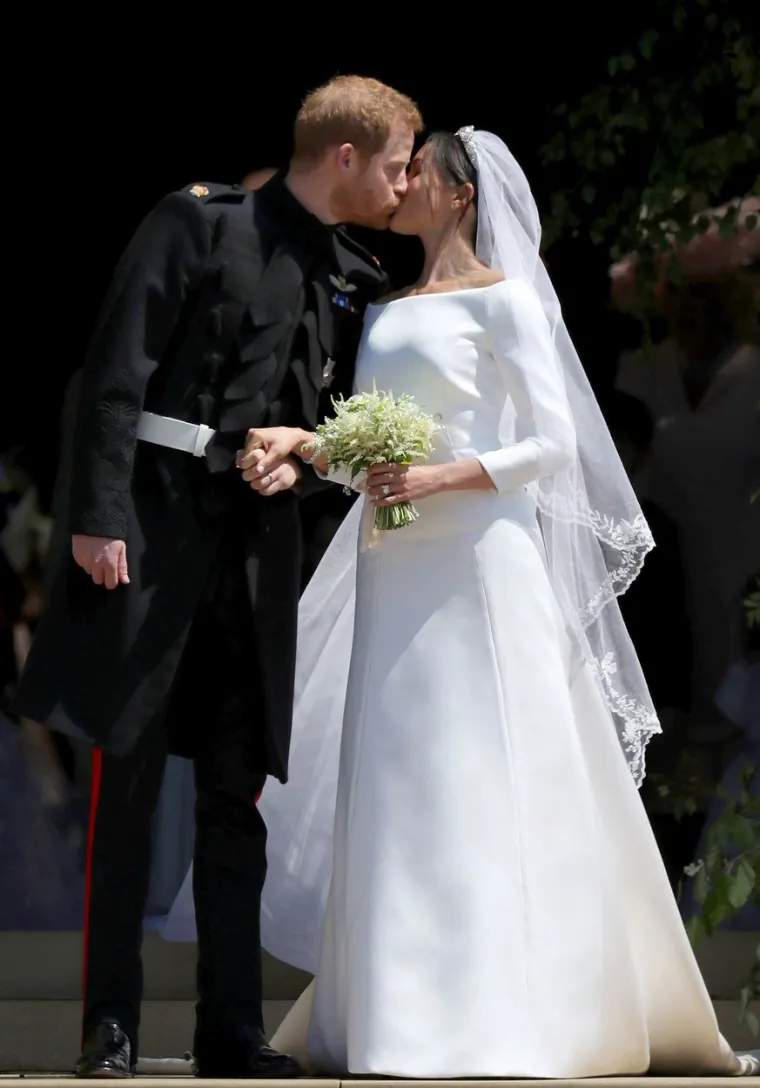 2018.: Meghan je na svoj veliki dan odjenula jednostavnu i bezvremensku vjenčanicu britanske dizajnerice Clare Waight Keller brenda Givenchy. Vjenčanica je bila izrađena od čiste bijele svile, koja je imala otvoreni dekolte. U ožujku 2016., prije nego što su se upoznali Meghan i Harry, glumica je rekla da je njezina najdraža vjenčanica svih vremena pripadala Carolyn Bessette-Kennedy, od njezina vjenčanja s Johnom F. Kennedyjem iz 1996. godine. 
