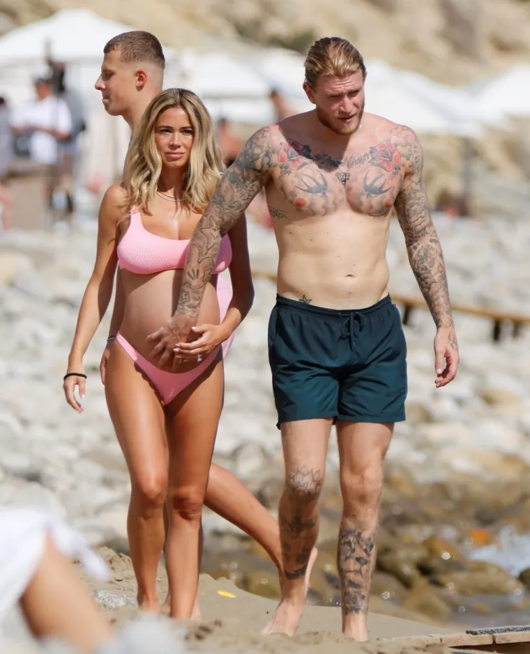Atraktivna voditeljica privlači poglede i upija zrake sunca na plaži, a njezin dragi uz nju zijeva