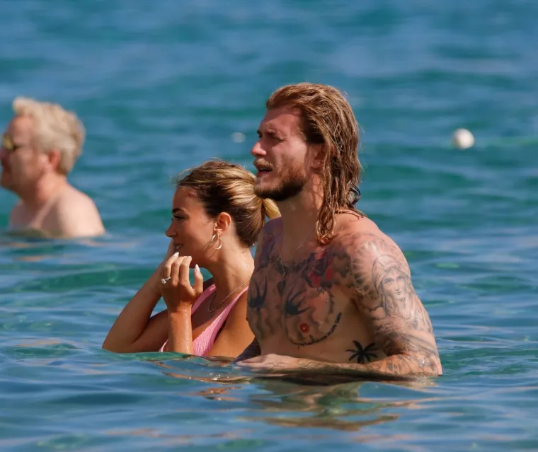 Atraktivna voditeljica privlači poglede i upija zrake sunca na plaži, a njezin dragi uz nju zijeva