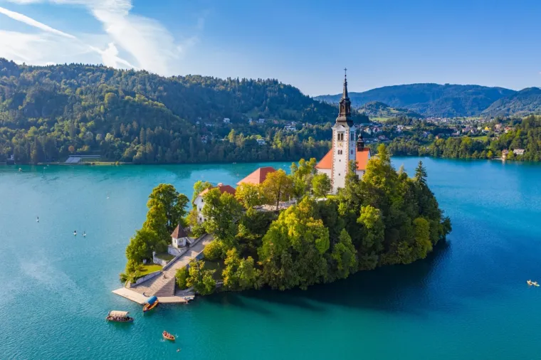 BLEDSKO JEZERO (SLOVENIJA) - Jedno je od najpoznatijih prirodnih znamenitosti Slovenije i pravi biser alpske regije. Smješteno u blizini Julijskih Alpa, okruženo je bujnim zelenilom, strmim planinama i planinskim vrhovima, što stvara romantičan i gotovo bajkovit pejzaž. Na sredini jezera nalazi se maleni otočić s crkvom Uznesenja Marijina, do kojeg posjetitelji mogu doći tradicionalnim čamcima poznatim kao pletne. Iznad jezera uzdiže se i bledski dvorac, srednjovjekovna tvrđava smještena na visokoj litici, koja nudi spektakularan pogled na cijelo jezero i okolnu prirodu. Bledsko jezero poznato je i po kremšnitama – kremastoj slastici koja je postala zaštitni znak ovog predivnog mjesta.