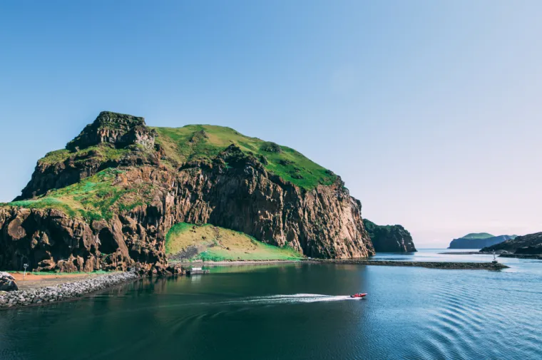 VESTMANNAEYJAR (ISLAND) - Arhipelag je od 15 vulkanskih otoka smještenih uz južnu obalu Islanda. Najveći i najpoznatiji otok je Heimaey, jedini naseljeni, poznat po svojoj teškoj povijesti erupcija i prirodnim ljepotama. Godine 1973. Heimaey je bio pogođen erupcijom vulkana Eldfell, koja je uništila dio grada i trajno promijenila izgled otoka. Danas je ta vulkanska prošlost dio identiteta Vestmannaeyjara, a posjetitelji mogu istražiti očuvane ostatke grada zatrpanog lavom i pepelom, što je danas dio muzeja na otvorenom.
Također, poznat je po bogatom ptičjem svijetu, uključujući kolonije puffina (atlantskih papiga), koje se gnijezde na liticama otoka. Svakog ljeta, otočani spašavaju mlade puffine koji zalutaju u grad umjesto prema moru.