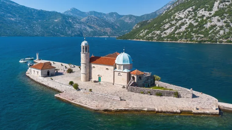 GOSPA OD &Scaron;KRPJELA (CRNA GORA)- prekrasan je umjetni otočić u Bokokotorskom zaljevu, kod grada Perasta u Crnoj Gori. Legenda kaže da je otočić nastao nakon &scaron;to su lokalni ribari 1452. godine prona&scaron;li ikonu Djevice Marije na stijeni u moru. Od tada su, kao zavjet, stoljećima bacali kamenje i potapali brodove s kamenjem na to mjesto, stvarajući otočić na kojem su izgradili crkvu posvećenu Gospi.
Ova barokna crkva, izgrađena u 17. stoljeću, čuva vrijedne umjetnine, uključujući oltarsku sliku majstora Tripa Kokolje, kao i kolekciju zavjetnih darova mornara koji su tražili za&scaron;titu Gospe. Svake godine, 22. srpnja, održava se tradicionalna ceremonija "Fa&scaron;inada", kada lokalni stanovnici dolaze brodovima i nastavljaju običaj bacanja kamenja oko otočića. 