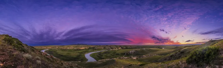 Zalazak sunca u Writing-on-Stone Provincial Parku u Alberti, Kanada, prikazuje rijeku Milk koja se uvija oko pješčenjaka. U daljini su planine Sweetgrass u Montani. 