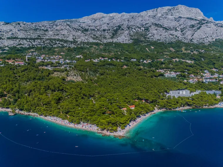 4. Punta Rata, Brela: Smještena u Brelima, na Makarskoj rivijeri, poznata je po Brela kamenu, stijeni koja izranja iz mora i prekrivena je borovima. Plaža je šljunčana, okružena borovom šumom, a more je kristalno čisto. Popularne aktivnosti uključuju snorkeling, kajakarenje, stand-up paddleboarding, pedaliranje, parasailing i jet ski. Uz obalu se nalazi šetnica s brojnim barovima i restoranima.