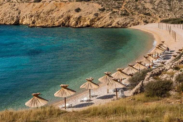 12. Oprna, otok Krk: Plaža Oprna, na otoku Krku, udaljena je pet minuta vožnje od Stare Baške. Skrivena je u uvali, a mirno more idealno je za početnike i djecu. Do plaže se može doći brodom ili pješačenjem oko 10-15 minuta niz strmu i često sklisku stazu. Na plaži se mogu iznajmiti ležaljke i suncobrani, a Oprna Beach Bar nudi hranu i piće.