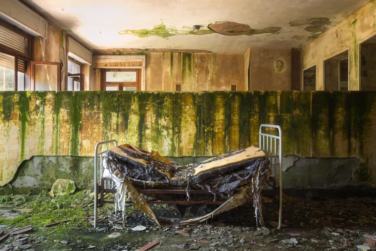 NAPUŠTENA BOLNICA U ITALIJI -  krije priču koja istovremeno oduzima dah i budi tihu jezu. Izgrađena je krajem 19. stoljeća, bolnica je prvotno služila kao sanatorij za djecu oboljelu od tuberkuloze, ali i općenito za prevenciju i liječenje bolesti dišnog sustava – tada čestih i često kobnih. Zgrada je podijeljena na tri etaže, a posebnu pažnju privlači mali prostor za duhovnu obnovu – kapelica s minijaturnom sakristijom, smještena na drugom katu. Iako je danas obrasla u prašinu, teško je ne zamisliti trenutke kada su se tamo okupljala djeca, bolesna, ali puna nade, u tihoj molitvi za ozdravljenje.
Tijekom Drugog svjetskog rata, točnije 1944. godine, partizani su rekurirali zgradu i pretvorili je u privremenu bolnicu za evakuaciju ranjenika i onih koji su bježali pred nacifašističkim trupama. Zidovi ove bolnice, već obilježeni mukom, tada su svjedočili još jednom valu patnje – ratu, ranama i gubicima.
Nakon rata, kompleks se ponovno vraća svojoj izvornoj namjeni. Postaje specijalizirana ustanova za liječenje respiratornih bolesti, ponajviše tuberkuloze, a u toj funkciji ostaje do kasnih 60-ih godina prošlog stoljeća, kada je, zbog razvoja moderne medicine i promjene potreba, zauvijek zatvorena.
Ono što je uslijedilo bila je tiha, ali neumoljiva propast. Desetljećima je bolnica bila u stanju progresivnog napuštanja. Kiša, vjetar i vrijeme učinili su svoje. Namještaj je ostao na mjestu, ali razbijeni prozori, oguljeni zidovi i urušeni stropovi danas svjedoče o neumoljivom zubu vremena.