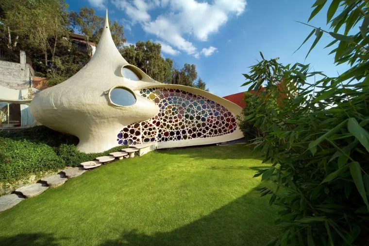 NAUTILUS HOUSE, MEKSIKO - Smještena u blizini Mexico Cityja, Nautilus House izgleda kao da je isplivala ravno iz bajke – ili s dna mora. Inspirirana oblikom morske školjke, ova jedinstvena građevina djelo je meksičkog arhitekta Javiera Senosiana, poznatog po stvaranju &quot;organske arhitekture&quot; koja imitira prirodne oblike i tokove.
Kuća je građena u potpunosti od armiranog betona, a njezini spiralni zidovi, šareni mozaici i obline bez oštrih rubova stvaraju dojam da ste zakoračili u neki drugi svijet – gotovo kao da se nalazite unutar živog bića. Unutrašnjost kuće prati isti fluidan, organski stil, s podovima prekrivenim biljkama i prozračnim prostorijama koje povezuju prirodu i arhitekturu na gotovo meditativan način.