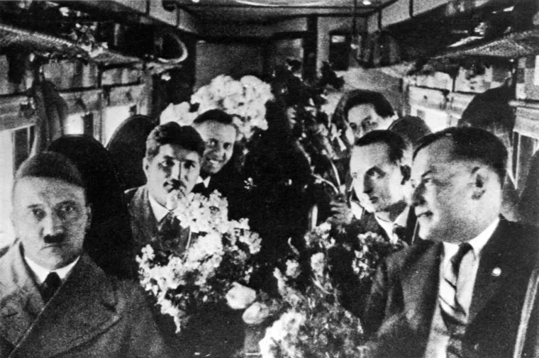 Intrigantna fotografija, pretpostavlja se da je snimljena u avionu 1925. Na fotografiji su svi osim Hitlera dobro raspoloženi. S njim su, slijeva nadesno na fotografiji: Julius Schreck, Julius Schaub, Ernst &apos;Putzi&apos; Hanfstaengl, Otto Dietrich (Hitlerov šef za štampu) i Wilhelm Brückner, pobočnik. 