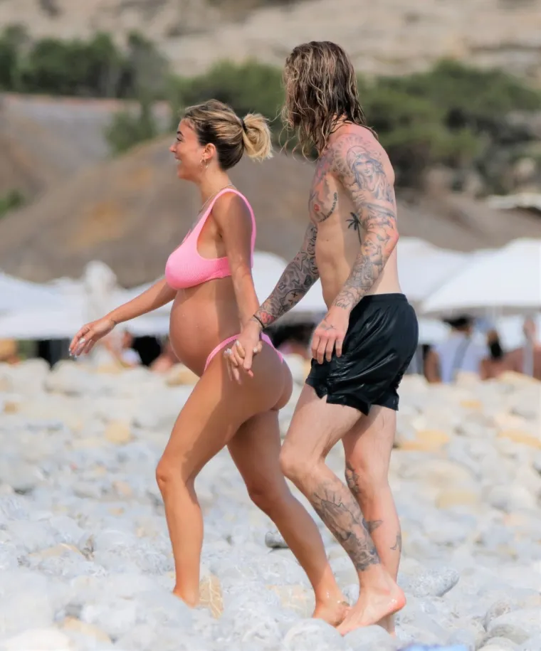 Atraktivna voditeljica privlači poglede i upija zrake sunca na plaži, a njezin dragi uz nju zijeva