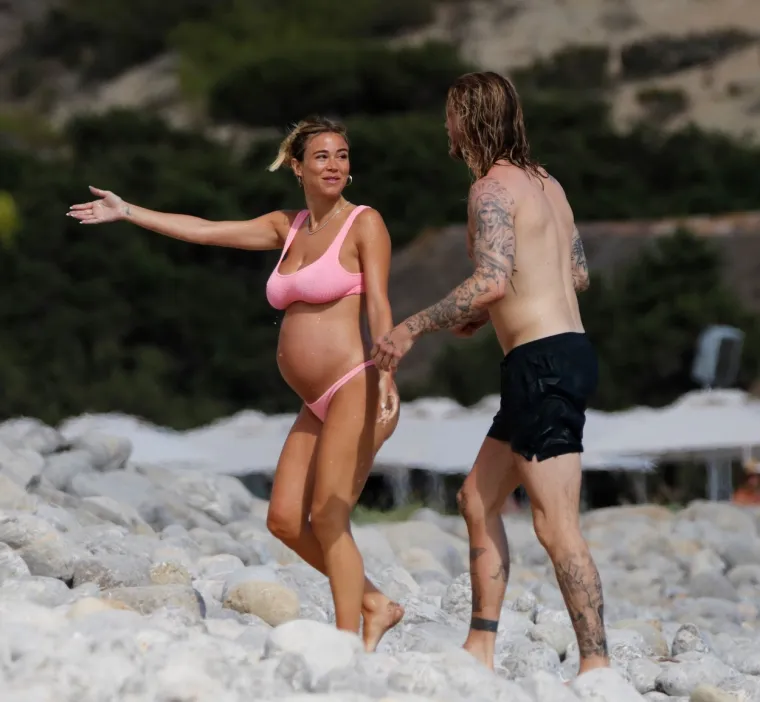 Atraktivna voditeljica privlači poglede i upija zrake sunca na plaži, a njezin dragi uz nju zijeva