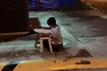 Maleni beskućnik piše zadaću na cesti uz svjetlo iz restorana