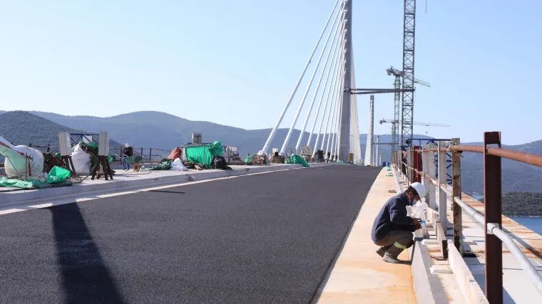 Konačno i prvi sloj asfalta na Pelje&scaron;kom mostu. Ali, postavlja se od sredine prema kopnu, a to i nije običan asfalt